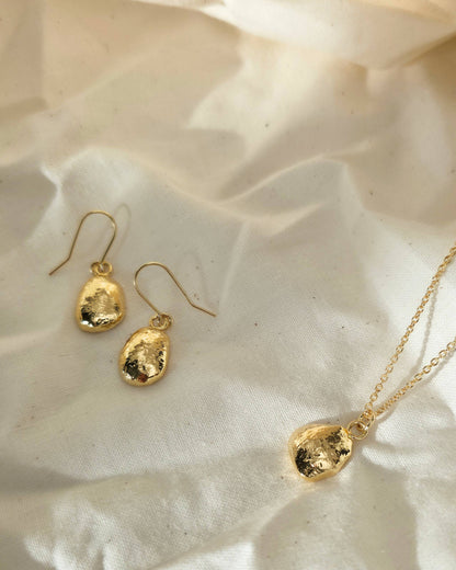 Gold oval shaped earrings and necklace on a beige surface