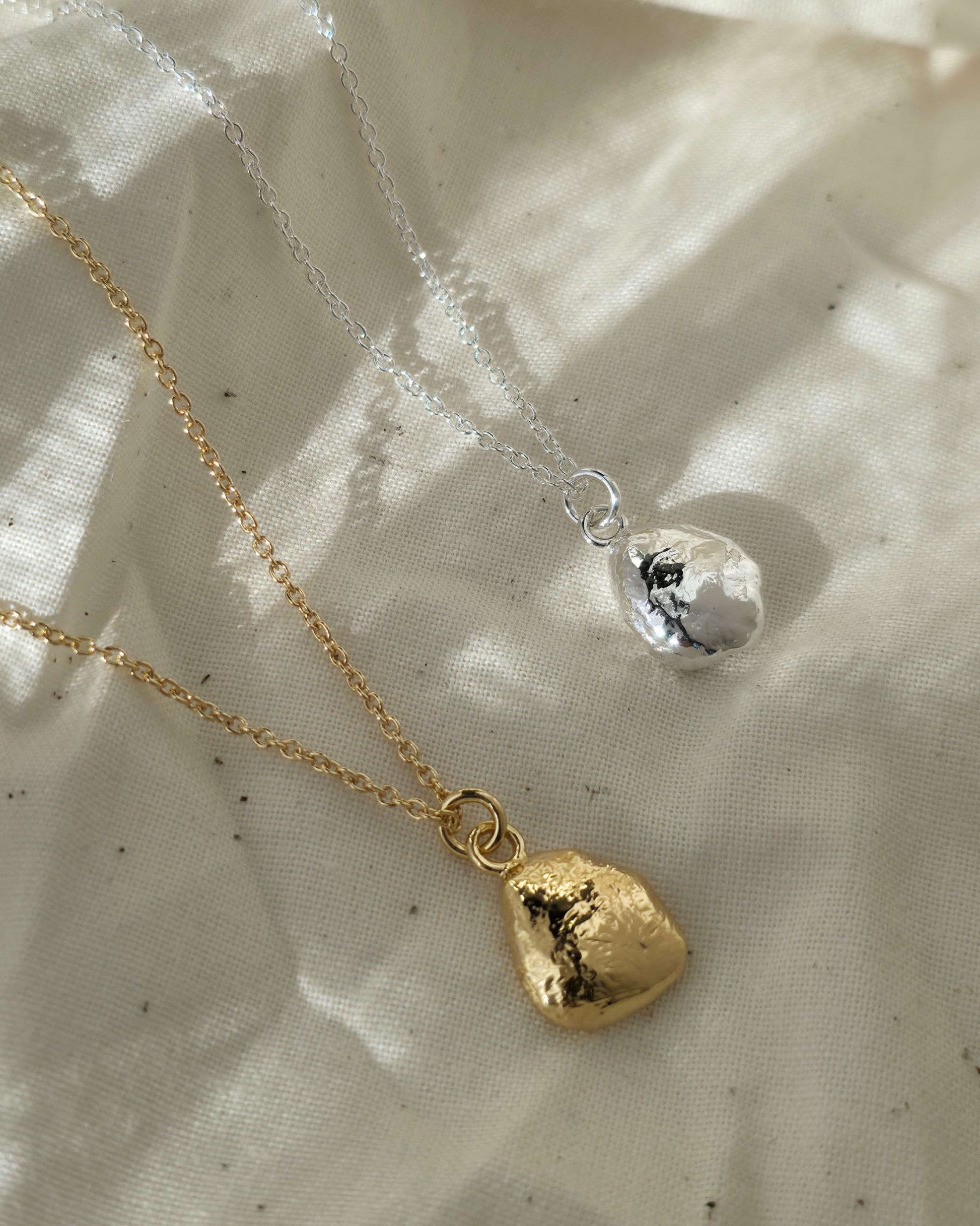 Gold and silver pendant necklaces lying in sunshine on beige fabric