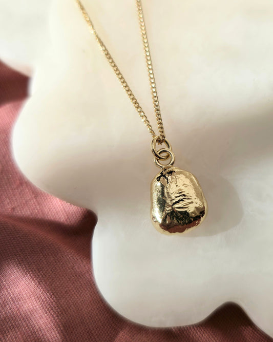 Textured gold pebble pendant lying on a cream background