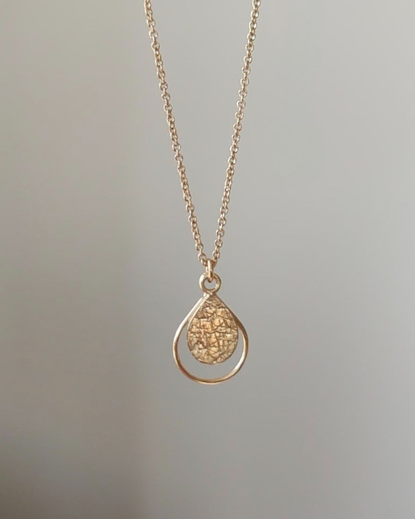 Gold necklace with a textured teardrop-shaped pendant on a light gray background