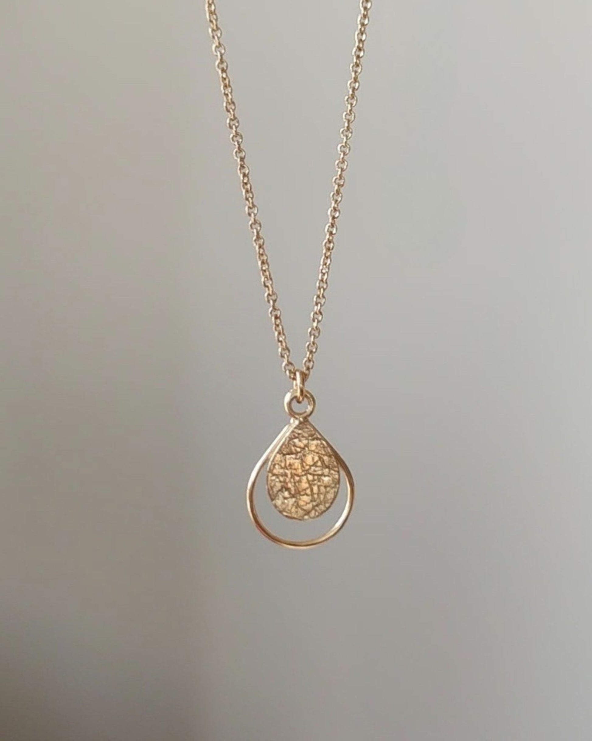 Gold necklace with a textured teardrop-shaped pendant on a light gray background
