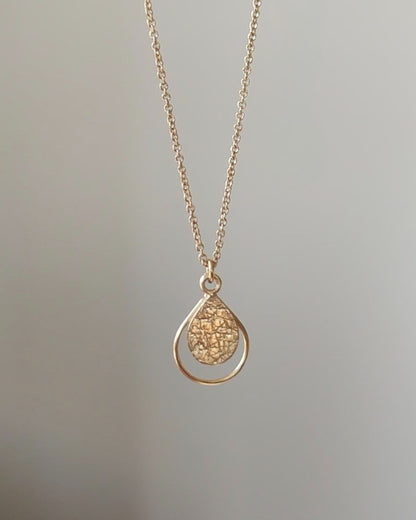 Gold necklace with a textured teardrop-shaped pendant on a light gray background