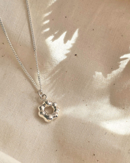 Unique molten silver pendant lying in shade on beige fabric with interesting shadows in background