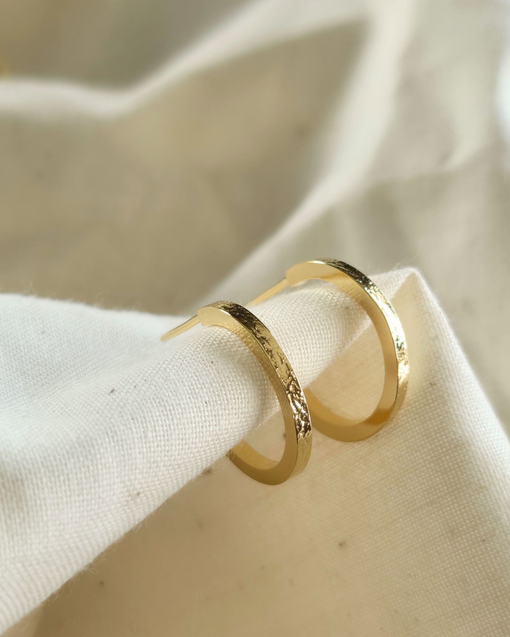 small gold textured hoop earrings on beige fabric background