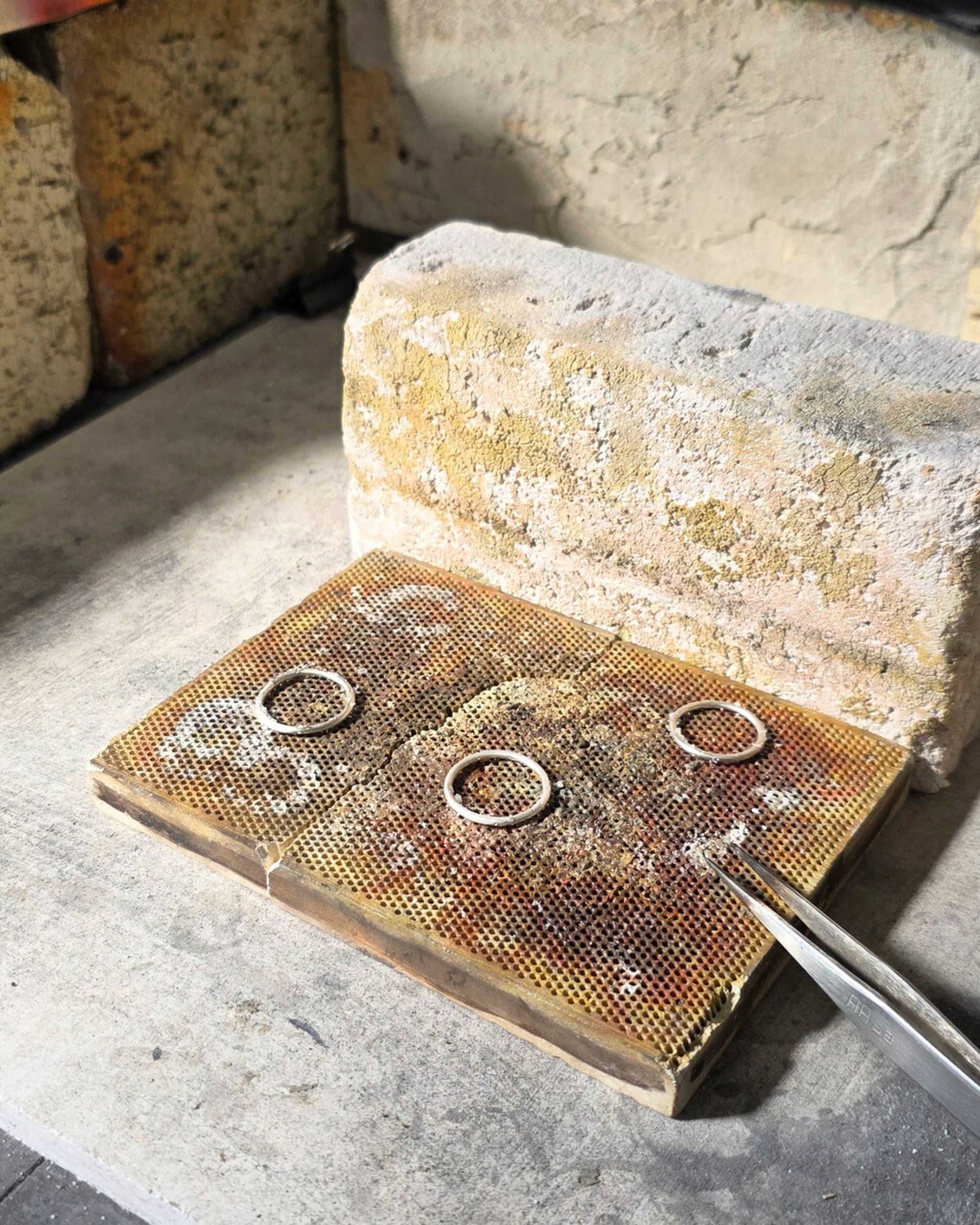 Three silver rings lying on a soldering block in a jewellery workshop setting