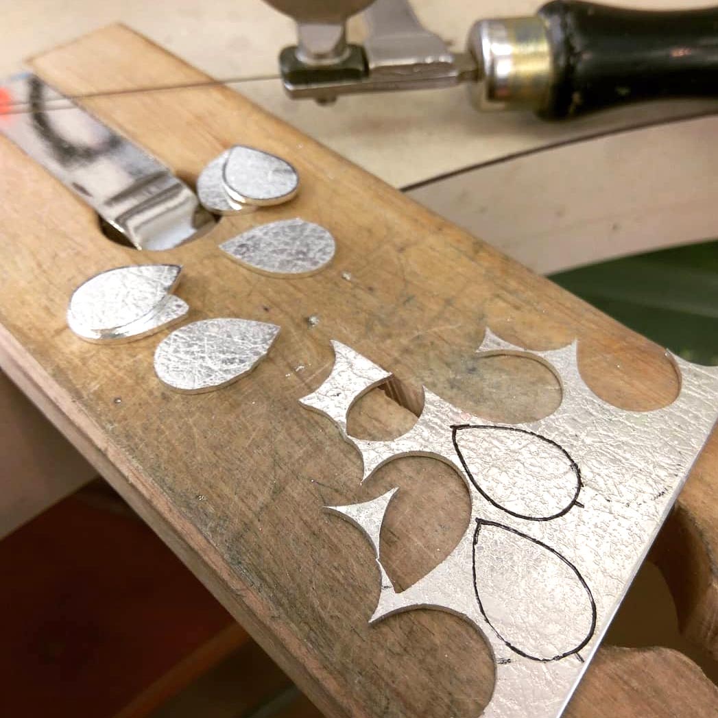 Piece of textured silver sheet with teardrop-shaped cutouts lying on wooden bench peg on jewellers bench