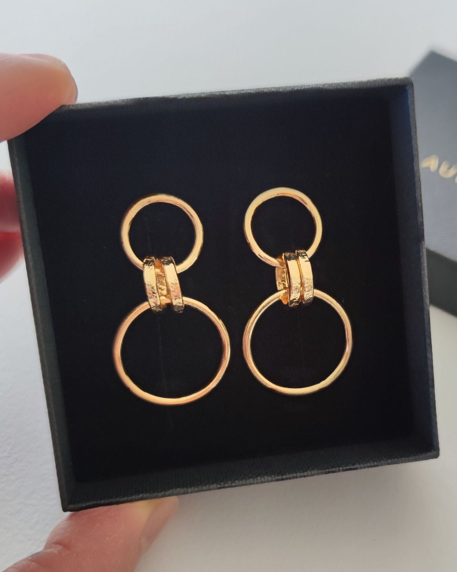 Close up of fingers holding black gift box containing gold drop earrings made from small and large loops