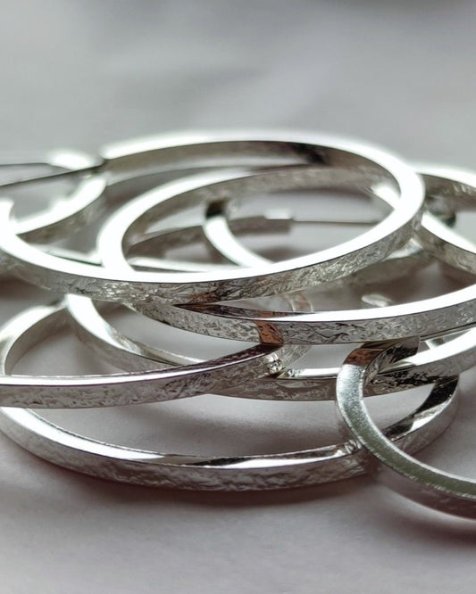 Pile of small and large textured sterling silver hoop earrings lying on grey surface