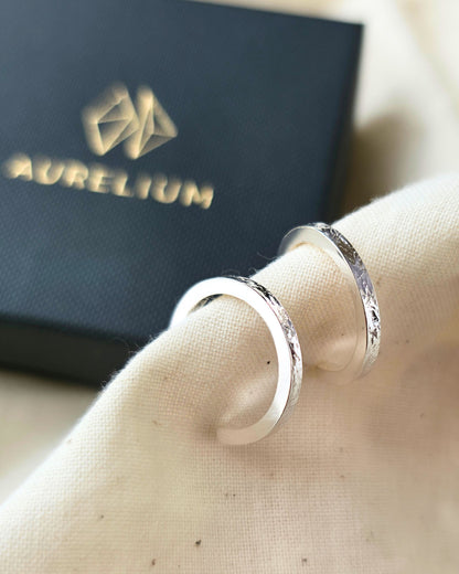 Minimalist textured silver hoop earrings on beige fabric with black Aurelium gift box in background