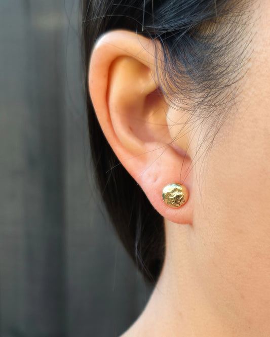 Close up of a person wearing a molten gold stud earring