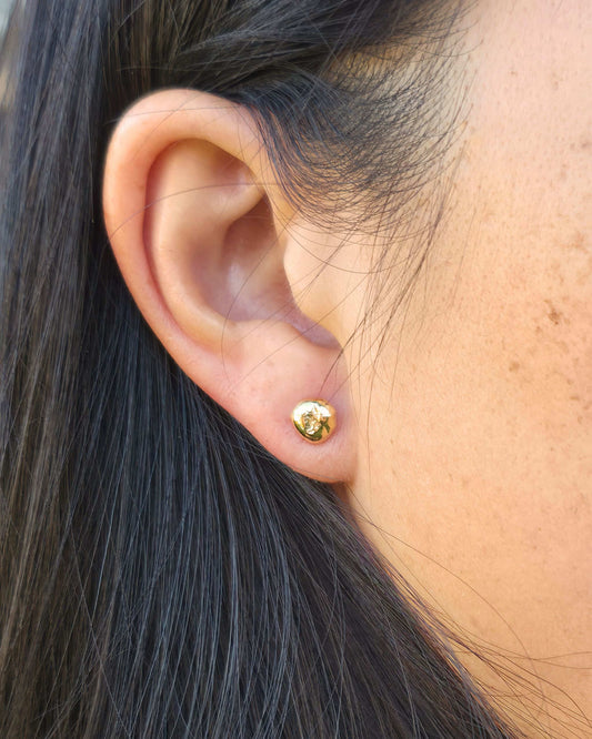 Close-up of a person wearing a small molten gold stud earring
