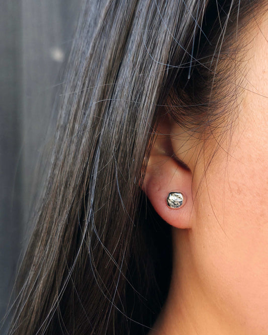 Close up of a person wearing a small molten sterling silver stud earring