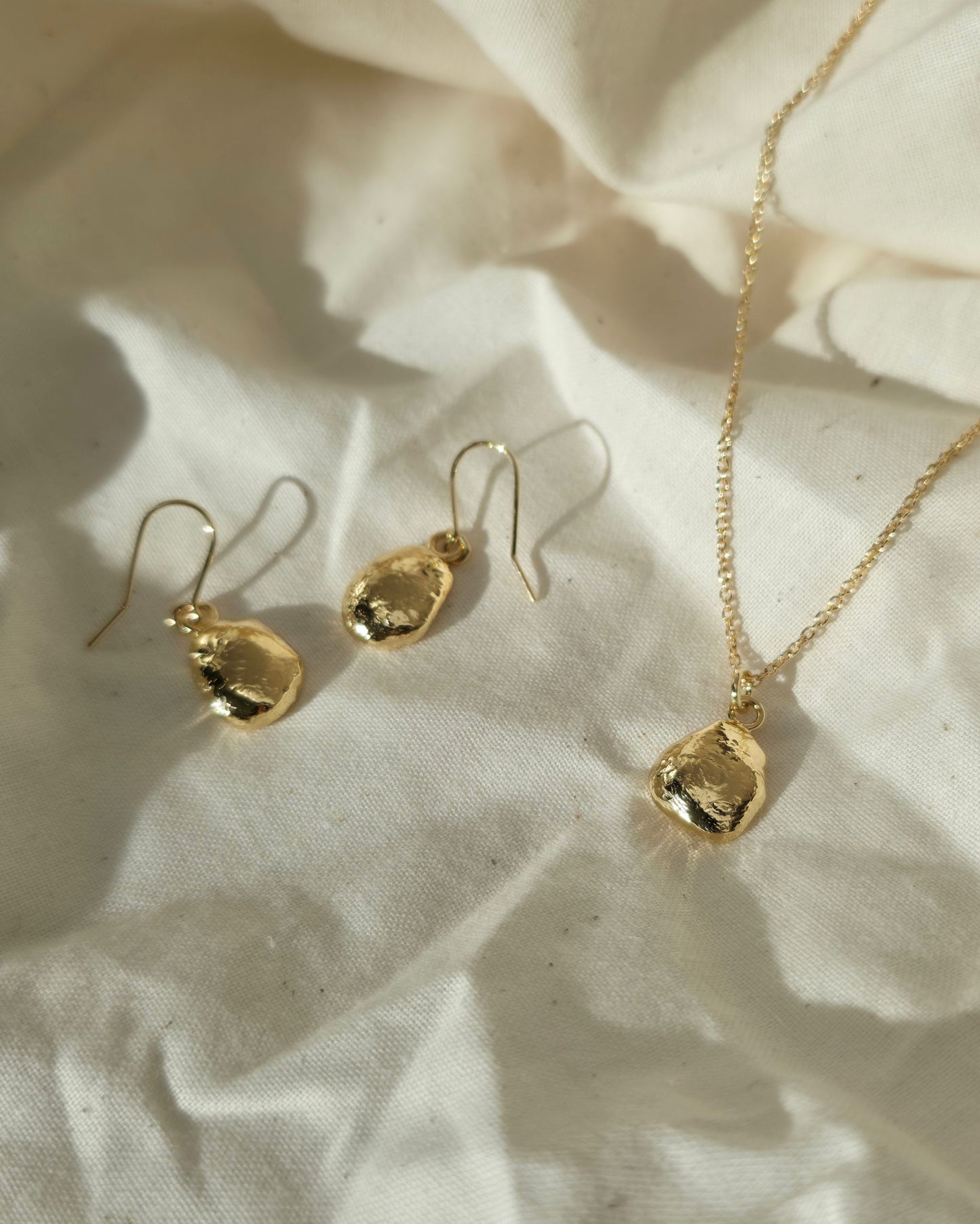 Gold jewelry set with earrings and a necklace on a textured beige fabric background
