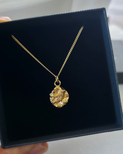 Gold pendant with a textured surface attached to delicate gold chain in black gift box