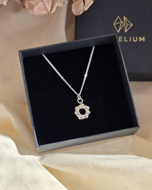 Molten silver pendant in flower shape arranged in black gift box with flower petals in background