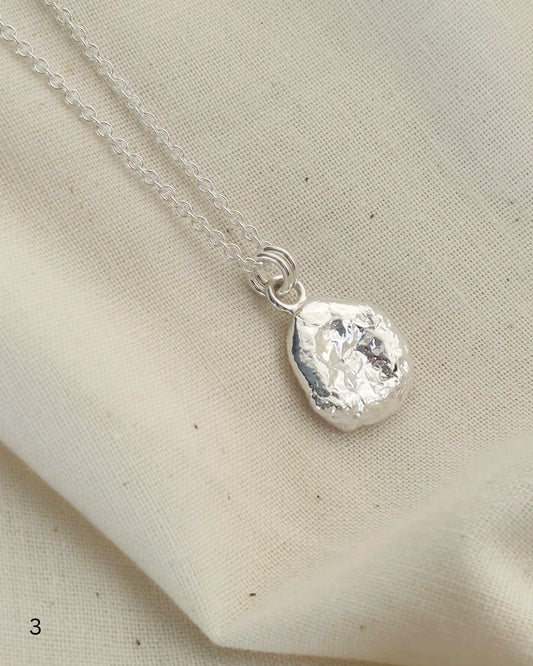 Round sterling silver pendant with textured surface on beige fabric background