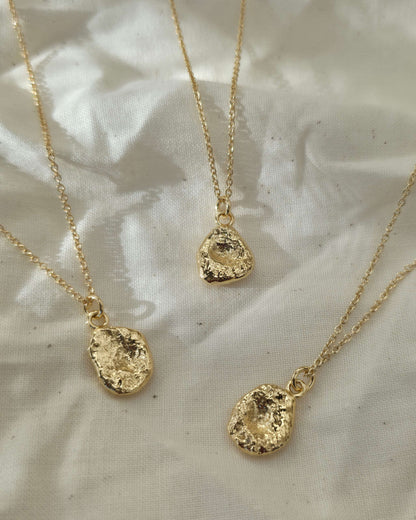 Three gold necklaces with textured pendants lying on cream coloured fabric