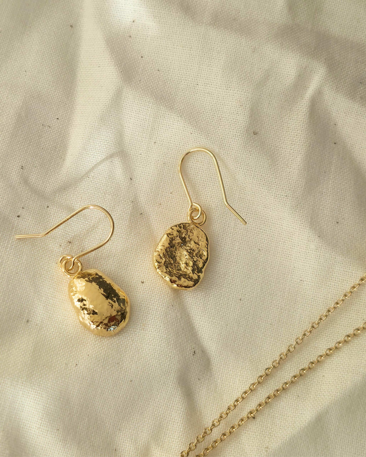 Gold oval shaped earrings with a textured surface lying on a beige fabric background