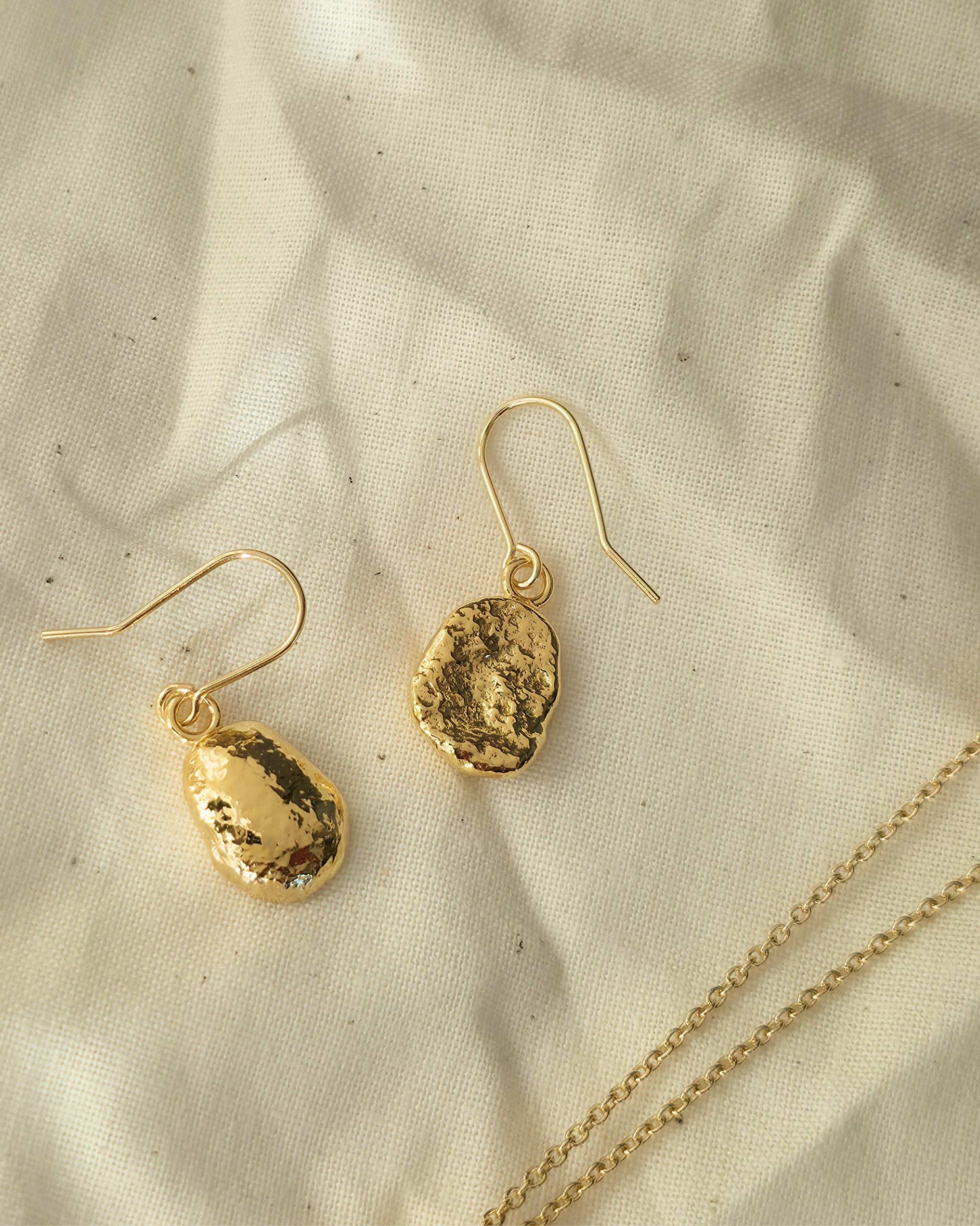 Gold oval shaped earrings with a textured surface lying on a beige fabric background