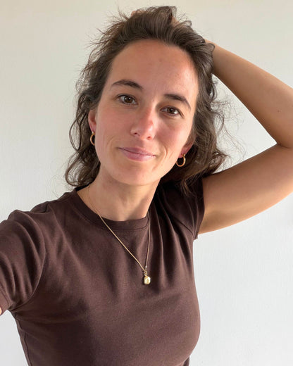 A woman wearing a brown teeshirt with small gold hoop earrings and a gold pendant