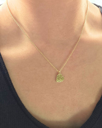 Close up of person wearing gold textured heart pendant necklace on delicate gold chain