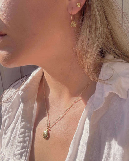 Close-up of a person wearing gold heart earrings and a gold oval necklace with a white shirt