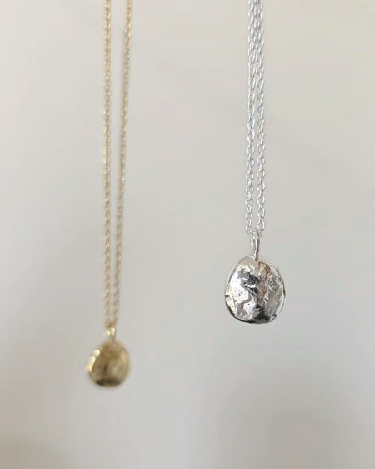 Two textured round pendant necklaces in gold and silver, hanging against a light background