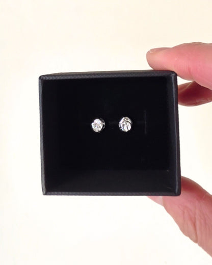 Small silver circle-shaped stud earrings in a black gift box held by a person's fingers