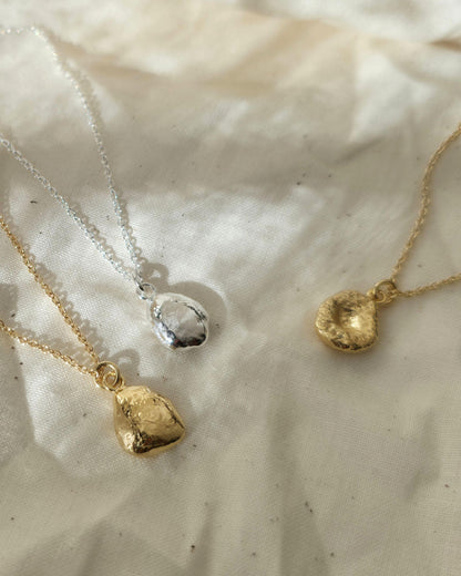Two gold necklaces and one silver necklace with textured pendants lying in sunshine on beige fabric
