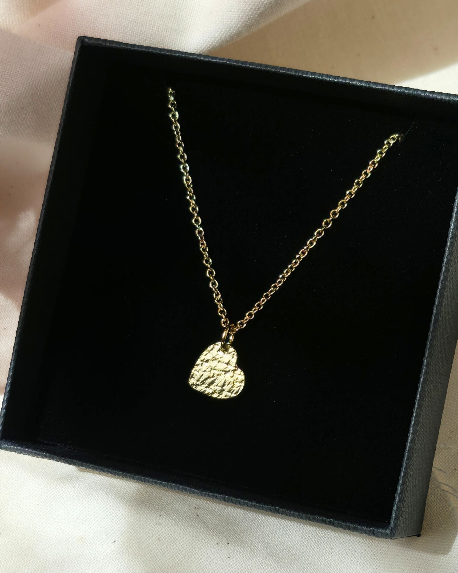 Gold necklace with a textured heart pendant in a black box