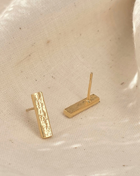 textured long gold bar stud earrings on fabric background