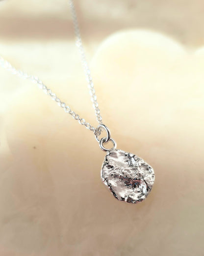 Silver necklace with a textured oval-shaped pendant on a blurred background