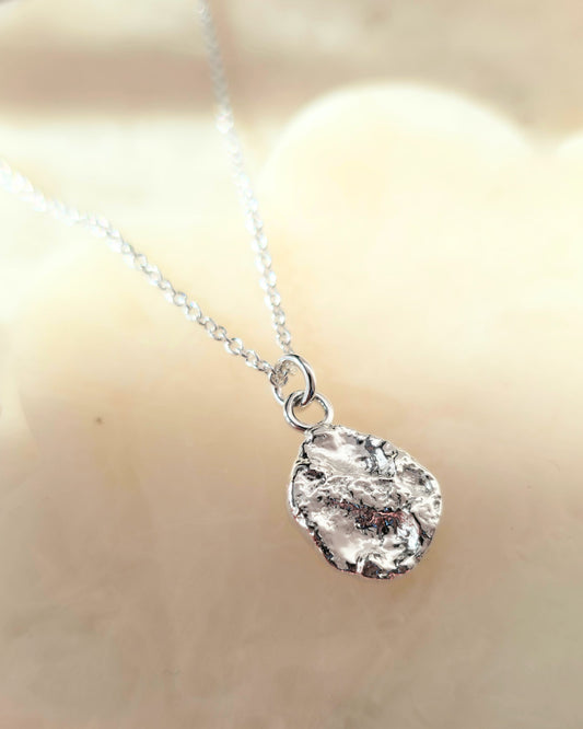 Silver necklace with a textured oval-shaped pendant on a blurred background