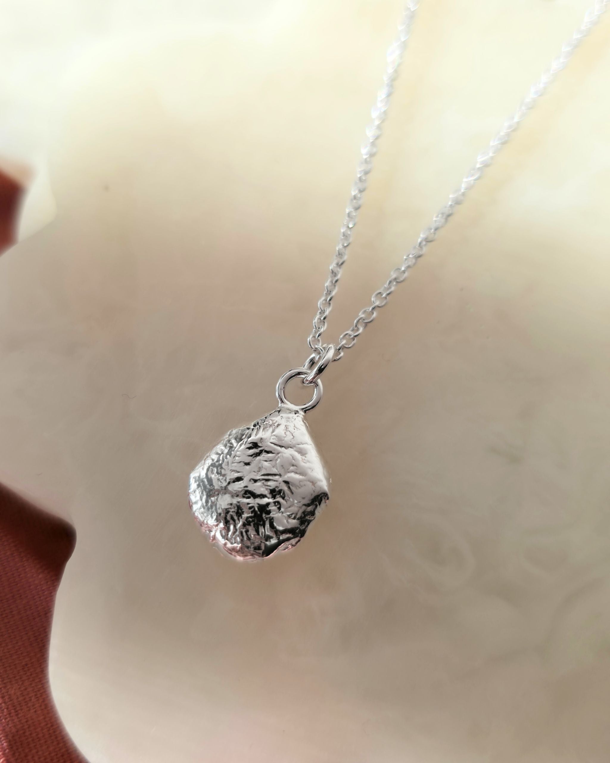 Silver necklace with a textured pendant on a neutral background