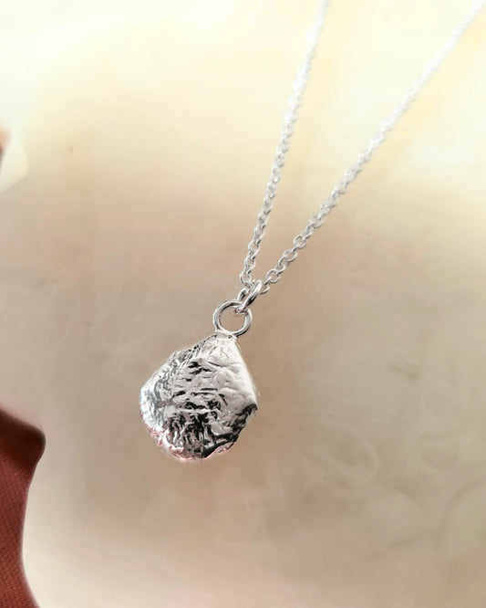 Silver necklace with a textured pendant on a cream surface
