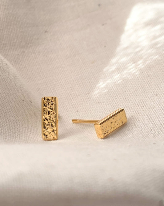 textured gold bar earrings on a pink and gray gradient background
