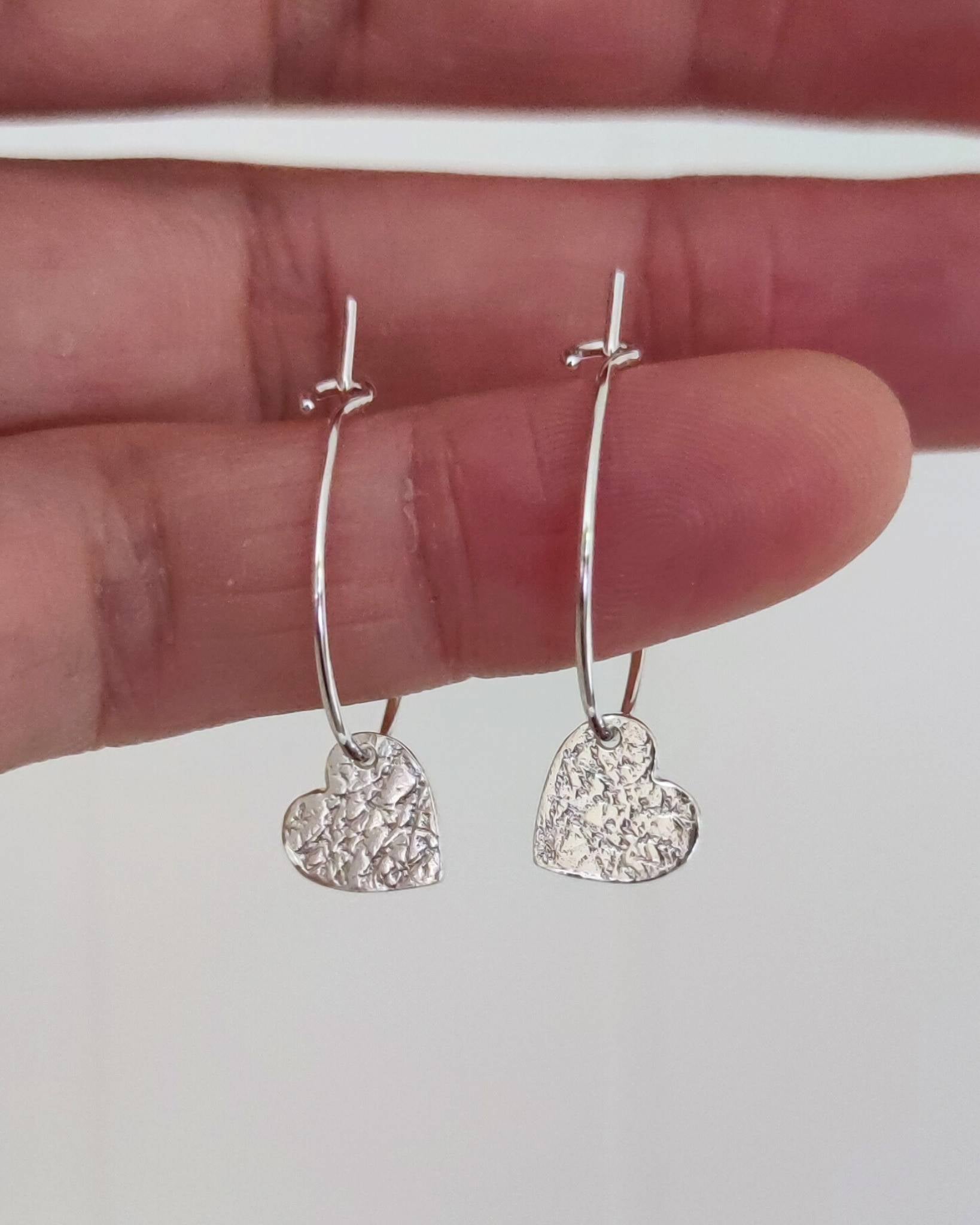 hand holding dainty textured sweetheart heart earrings in sterling silver