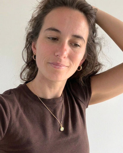 woman with brown hair wearing a dark brown tee-shirt, gold hoop earrings and a fine necklace with a small gold pendant