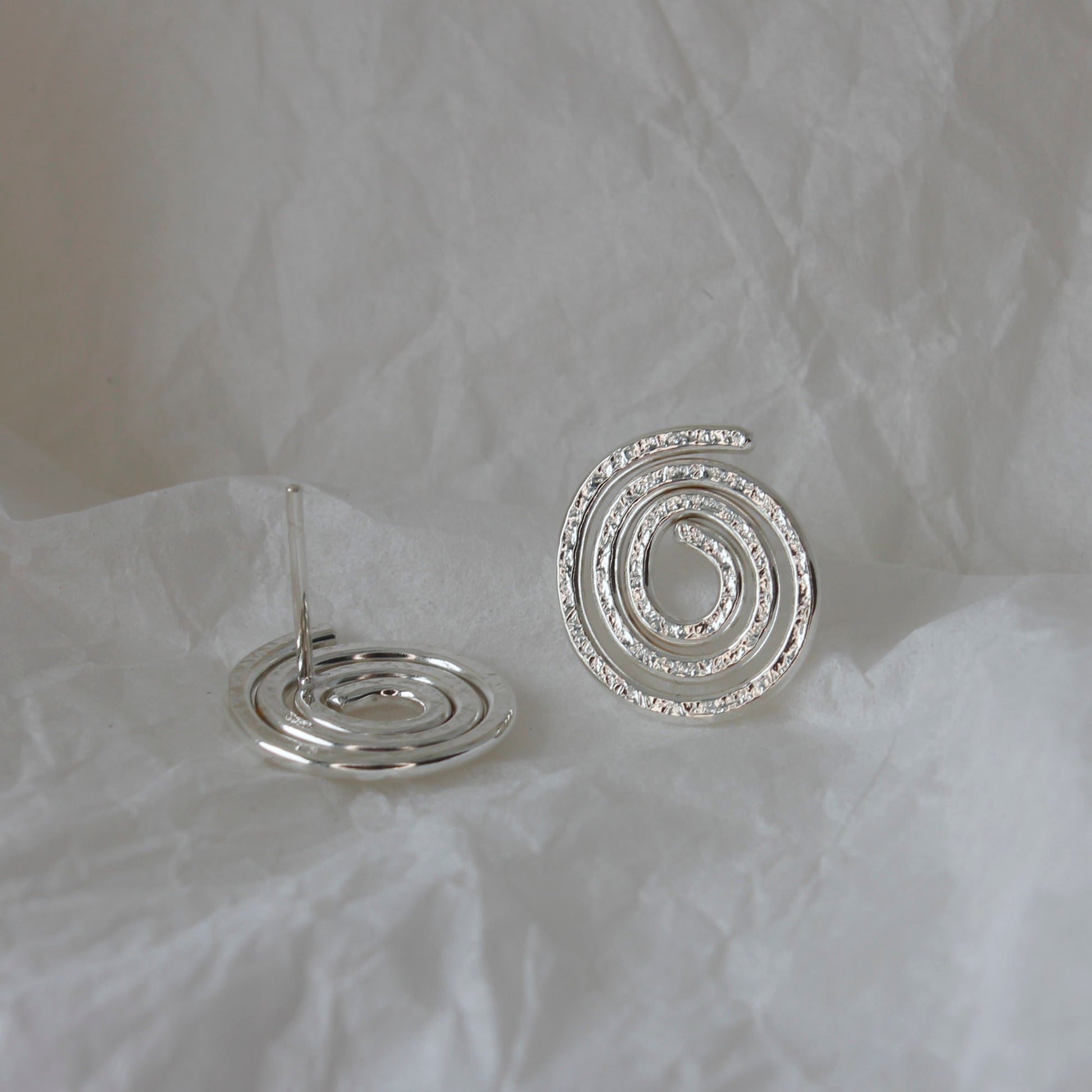 minimalist sterling silver swirl stud earrings lying on tissue paper