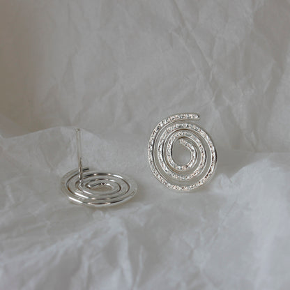 minimalist sterling silver swirl stud earrings lying on tissue paper