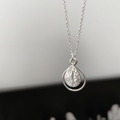 sterling silver dewdrop necklace by aurelium suspended in front of jewellery workbench