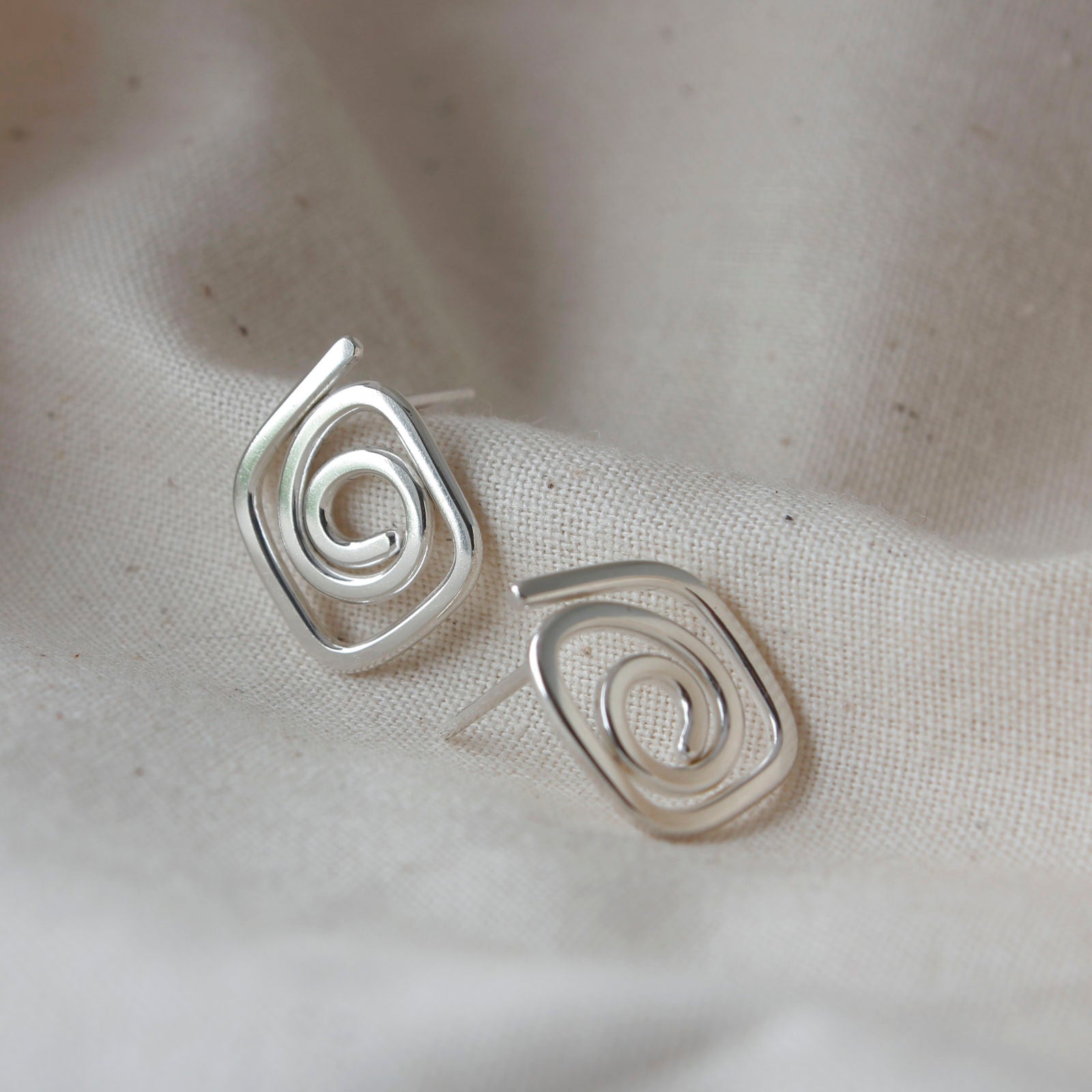 handmade silver diamond swirl earrings lying on cream fabric